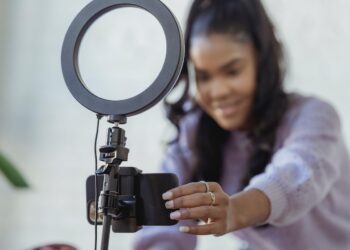 Happy young black woman setting up smartphone before shooting podcast | FintechZoom