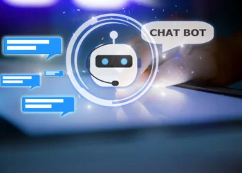 A glowing AI chatbot icon with a robotic face and headset is surrounded by blue chat bubbles. To the right, a hand interacts with a tablet screen. Above the chatbot icon, a speech bubble says, "CHAT BOT." The background is dark with blue light effects. | GRAMHIR