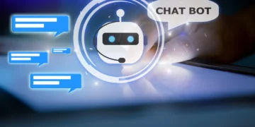 A glowing AI chatbot icon with a robotic face and headset is surrounded by blue chat bubbles. To the right, a hand interacts with a tablet screen. Above the chatbot icon, a speech bubble says, "CHAT BOT." The background is dark with blue light effects. | GRAMHIR