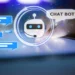 A glowing AI chatbot icon with a robotic face and headset is surrounded by blue chat bubbles. To the right, a hand interacts with a tablet screen. Above the chatbot icon, a speech bubble says, "CHAT BOT." The background is dark with blue light effects. | GRAMHIR