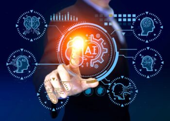 A person in a suit interacts with a virtual interface featuring an illuminated AI symbol at the center. Surrounding icons represent various elements of artificial intelligence, including brain graphics, gears, and personal finance charts, all set against a dark blue background. | GRAMHIR