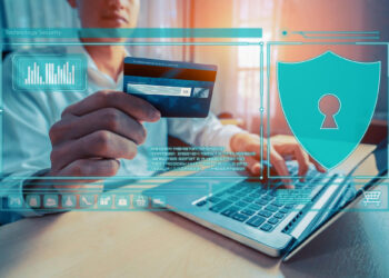 A person holds a credit card while using a laptop, mindful to protect their online identity. Digital icons, including a shield with a keyhole, float around them, symbolizing online security. A graph and shopping cart icon are also visible, highlighting e-commerce and data protection. | GRAMHIR