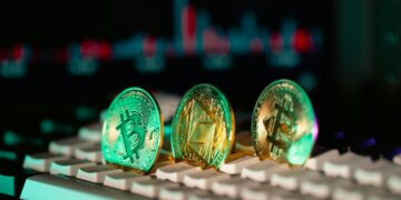Three cryptocurrency coins—Bitcoin, Ethereum, and Litecoin—stand upright on a computer keyboard, with a blurred digital graph in the background. The scene’s vivid lighting hints at debates like “Will AI Replace Crypto?” in the digital finance world. | GRAMHIR