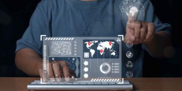 Person using virtual interface with world map, data graphics, and touch screen controls on a keyboard.
