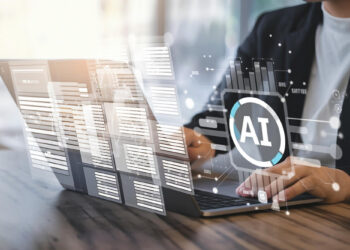 A person uses a laptop at a desk, with digital overlays of data, charts, and a large AI symbol on the screen, representing artificial intelligence technology. | GRAMHIR
